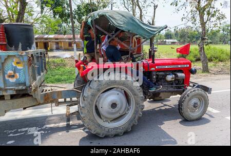 Scena di strada in Kaziranga, quartiere Golaghat, Bochagaon, Assam, India: persone locali alla guida di un rosso Massey Ferguson 1035 di trattore su strada Foto Stock