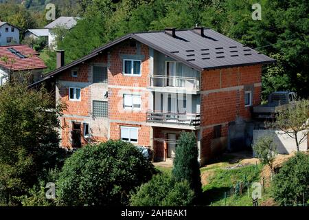 Incompiuta rossi e grandi blocchi di costruzione suburbana casa di famiglia con il nuovo tetto circondato con un fitto di alberi in caldo e soleggiato giorno di estate Foto Stock