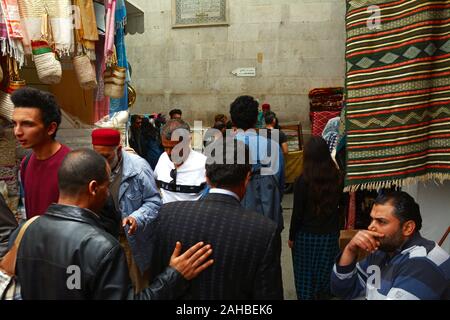 Una folla di locali di tunisini a piedi passato negozi di souvenir nel souk della Kasbah quartiere della Medina (città vecchia) di Tunisi, Tunisia. Foto Stock