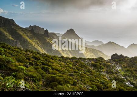 Spagna, Tenerife, montagne di masca canyon presso la costa dell'oceano, vista al di sopra natura verde paesaggio con Sun e oscura pioggia nuvole sul giorno di tempesta Foto Stock