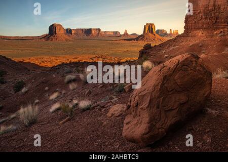 Artista del punto, Monument Valley, AZ a sunrise. La grande roccia rossa in primo piano scuro contrasta con l'Oriente Mitten Butte in background. Foto Stock