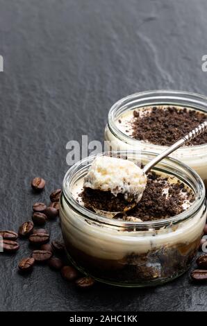 Layered cappuccino cremoso cheesecake in un barattolo di vetro nero su sfondo di pietra Foto Stock