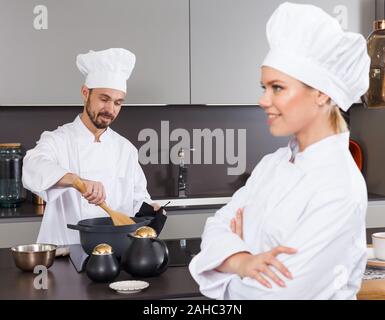 Fiducioso maschio personale chef in cucina arredamento moderno di cucina privata con il collega di sesso femminile in primo piano Foto Stock