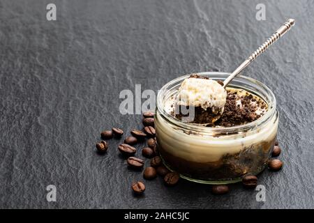 Layered cappuccino cremoso cheesecake in un barattolo di vetro nero su sfondo di pietra Foto Stock