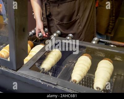Ripresa a tutto campo della trdelnik, una torta allo spiedo, cottura in un negozio a Praga Foto Stock