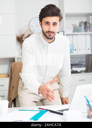 Amichevole maschio giovane lavoratore di ufficio con la mano estesa per stretta di mano in ufficio Foto Stock