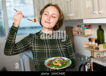 Donna positivo prepara la cena in cucina, tenendo la piastra di fresco con insalata di reso Foto Stock