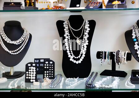 Varietà di collane, bracciali e orecchini in perle bianche e nere su manichini in negozio gioielli finestra Foto Stock