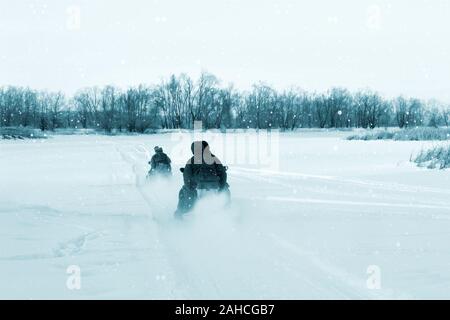 Gli uomini su due motoslitte andare sul fiume d'inverno. Vista dal retro Foto Stock