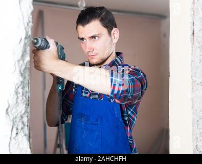 Calma professional builder foro di perforazione nella parete con un perforatore in una camera riparabile Foto Stock