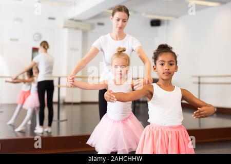 Giovani femmine di danza classica con insegnante aiutandola bambine gli studenti nella classe di balletto Foto Stock