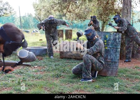 Paintball femmina giocatore in piena attrezzatura mirando con la pistola in sparatoria all'aperto Foto Stock