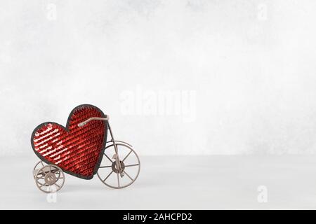 Toy bike portando grande cuore rosso. Il giorno di San Valentino del minimalismo sfondo. amore simbolo, spazio per il testo concetto. elemento di design per biglietti di auguri, vendita Foto Stock