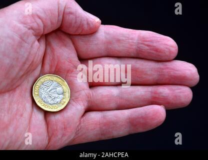 Uno britannico pound coin nel palmo di una mano di un uomo contro uno sfondo scuro Foto Stock