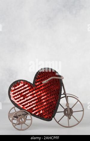 Toy bike portando grande cuore rosso. Il giorno di San Valentino del minimalismo sfondo. amore simbolo, spazio per il testo concetto. elemento di design per biglietti di auguri, vendita Foto Stock