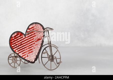 Toy bike portando grande cuore rosso. Il giorno di San Valentino del minimalismo sfondo. amore simbolo, spazio per il testo concetto. elemento di design per biglietti di auguri, vendita Foto Stock