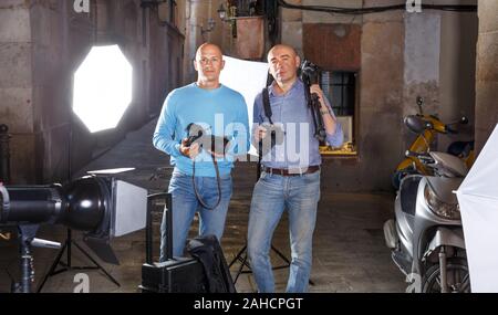 Ritratto di due fotografi di successo con le loro macchine fotografiche professionali durante le riprese fotografiche su una strada della città Foto Stock