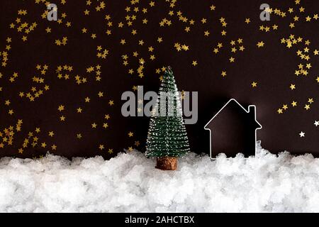 Natale in miniatura e casa sulla neve e uno sfondo scuro con stelle luccicanti con copia spazio. Composizione di natale, modello di cartolina Foto Stock