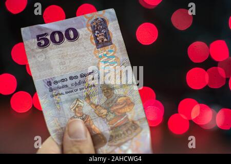 Mano trattiene un 500 Sri Lanka rupie nota banca valuta il denaro, rosa e rosso sfondo bokeh di fondo con copyspace Foto Stock