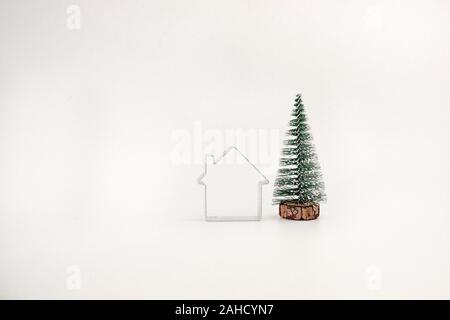 Miniatura coperte di neve albero di Natale e una semplice casa isolata su sfondo bianco Foto Stock