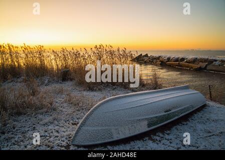 I primi raggi del sole sopra il lago Ladoga al mattino in inverno. Una barca rovesciata su una spiaggia innevata. Regione di Leningrado . Foto Stock
