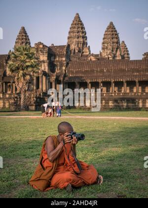 Monaco buddista in tradizionale accappatoio arancione scattare foto di fronte al tempio di Angkor Wat, Siem Reap, Cambogia Foto Stock