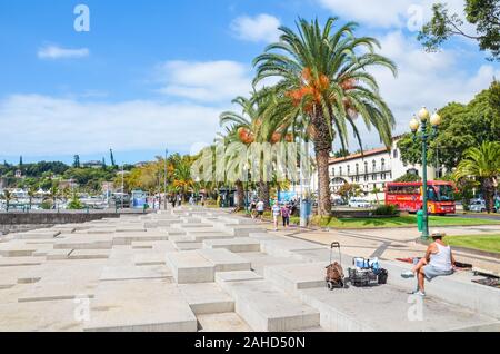 Funchal, Madeira, Portogallo - Sep 10, 2019: passeggiata del lungomare nel capitale di Madeira. La vegetazione verde, palme, un venditore ambulante e persone sulle strade. Soleggiata giornata estiva. La vita quotidiana. Foto Stock