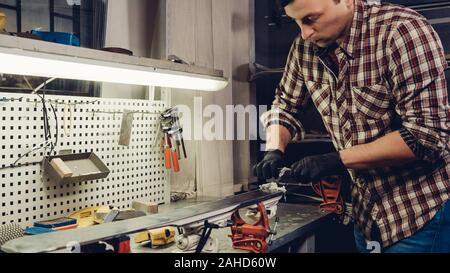 Manutenzione sci. Rimozione di eccesso di cera da gara di sci in plastica di base del raschiatore. Il servizio sci e riparazione. Inverno shop lavoratore che fa la riparazione di base. Workshop di noleggio Foto Stock