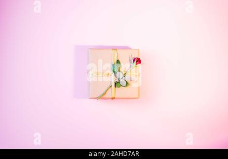 Piccola confezione regalo con little red rose e cuori attorno.presente avvolto con carta craft e decorate con un fiore. Sfondo rosa. Foto Stock
