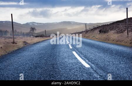 Durante un viaggio in Scozia - nero su strada asfaltata con montagne e brughiere in background Foto Stock