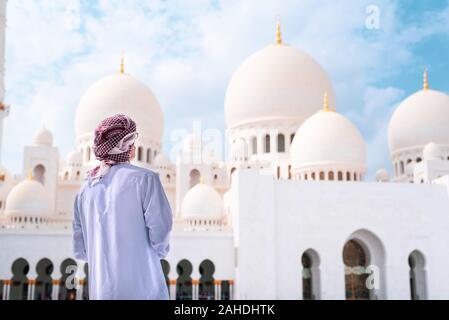 Uomo Arabo visitando la Grande Moschea di Abu Dhabi indossando vestiti tradizionali vista posteriore Foto Stock