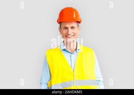 Uomo maturo indossare casco e unifrorm studio in piedi isolato su sfondo bianco cercando fotocamera a sorridere allegro Foto Stock