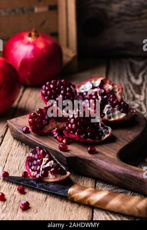 Fresche e mature melograni intero, aperto il melograno e semi in ciotola, coltello sulla tavola di legno, still life, close up Foto Stock