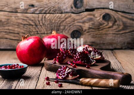Fresche e mature melograni intero, aperto il melograno e semi in ciotola, coltello sulla tavola di legno, still life, close up Foto Stock
