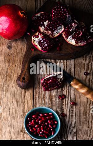 Fresche e mature melograni intero, aperto il melograno e semi in ciotola, coltello sulla tavola di legno, still life, close up Foto Stock