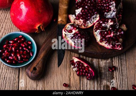 Fresche e mature melograni intero, aperto il melograno e semi in ciotola, coltello sulla tavola di legno, still life, close up Foto Stock