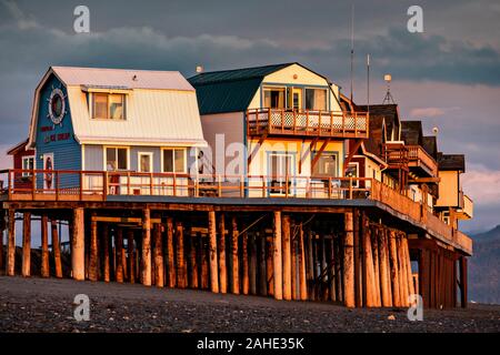 Il tramonto dei negozi e ristoranti di Homer Spit lungo la baia Kachemak in Omero, Alaska. Omero è noto come la fine della strada ed è circondato dal deserto e oceano. Foto Stock