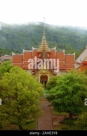 Vista in elevazione di un tempio buddista di Wat Chalong, situato in Phuket, Tailandia in un giorno di nebbia. Giungla lussureggiante possono essere visti sullo sfondo. Foto Stock