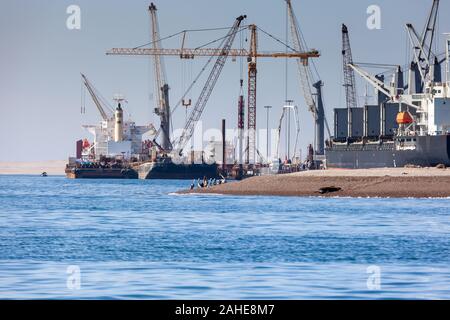 Paracas, Perù - 2019-12-05. Nel porto, cargo cranes sono il caricamento su una nave da carico. Gli uccelli possono essere visti sul berug contro lo sfondo della Foto Stock