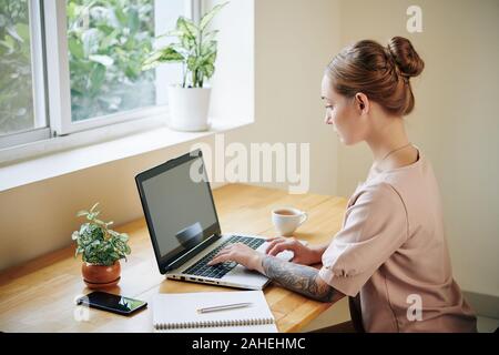 Studentessa lavorando laptop e iscritto nel libro di testo quando si fanno i compiti a casa Foto Stock