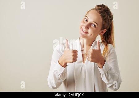 Ritratto di bella sorridente giovane donna che mostra pollice in su per esprimere approvazione Foto Stock