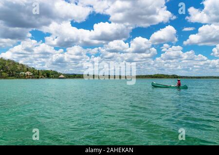 El Remate, Peten, Guatemala - 29 Maggio 2019: pescatore in canoa barca in color turchese del lago Itza lungo il villaggio con sunny cloud sky Foto Stock