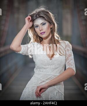 Bella giovane donna che indossa elegante abito bianco godendo le travi di luce celeste e fiocchi di neve che cadono sul suo viso. Bella bruna ragazza Foto Stock