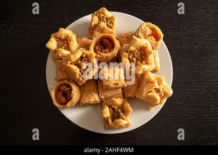 Tradizionale orientale il baklava assortiti. Vista dall'alto. Arabo dolci da forno in piastra bianca sul legno scuro tavolo. Baklawa mix Foto Stock