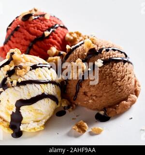 Tre palline di aromatizzati congelati gelato guarnita con noci tritate e spruzzata cioccolato in una vista ravvicinata Foto Stock