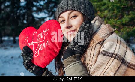 Il giorno di San Valentino. Giovane donna detiene il cuscino rosso a forma di cuore con I love you iscritto nella foresta di inverno Foto Stock