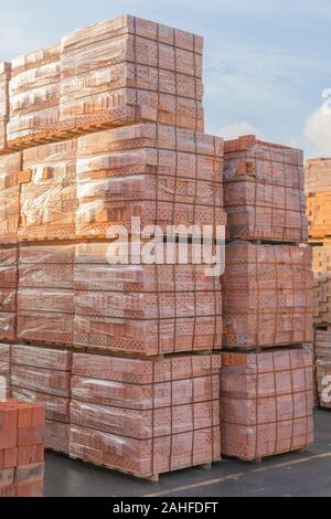 Diversi pallet con mattoni di cemento sovrapposti in magazzino. La produzione industriale di mattoni. foto verticale. Foto Stock