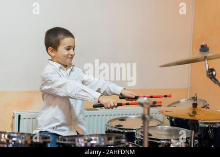 Boy drumming. ragazzo in una camicia bianca riproduce i tamburi. Foto Stock