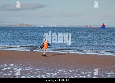 Portobello Beach, Edimburgo, Scozia, Regno Unito. Il 29 dicembre 2019. Milder temperatura a 11 gradi, ventilata con sole basso sulla costa di incoraggiare la gente ad uscire sulla spiaggia sabbiosa, un giovane ragazzo e suo padre ha fatto bene per ottenere i loro coloratissimi aquiloni e una moda donna indossa rosso brillante wellies con la sua Dalmazia e circondato da due altri cani. Foto Stock