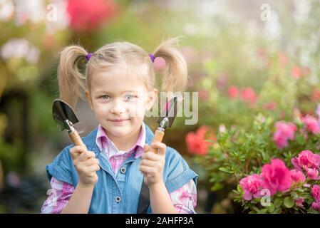 Bambino di piantare fiori di primavera in serra. Bambina giardiniere piante azalea. Bambino di prendersi cura di piante. Bambino con cesto fiorito. ragazza con Foto Stock